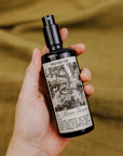Hand holding a bottle of 'Phantom Row' with a label featuring black and white imagery on a blurred background.