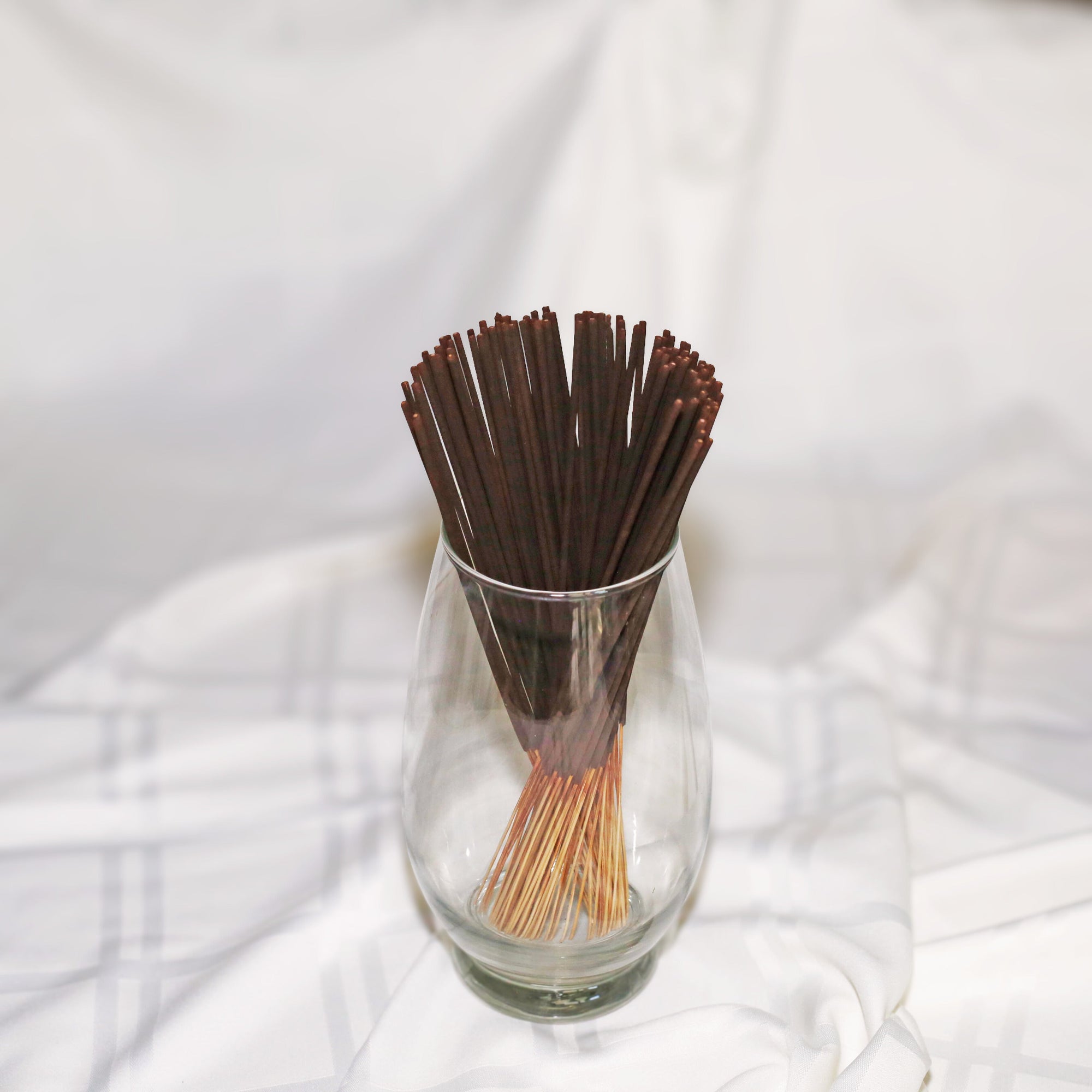 Glass vase with brown incense sticks on a white fabric background