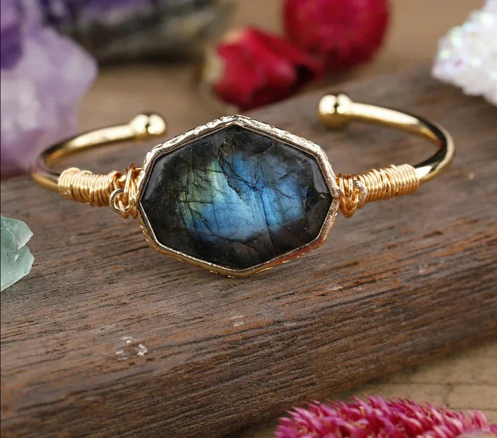Gold bracelet with a labradorite stone on a wooden surface with flowers in the background