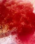 Heart-shaped bath bomb fizzing in rosy red  bath water with rose petals