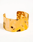 Gold cuff bracelet with textured surface on a white background
