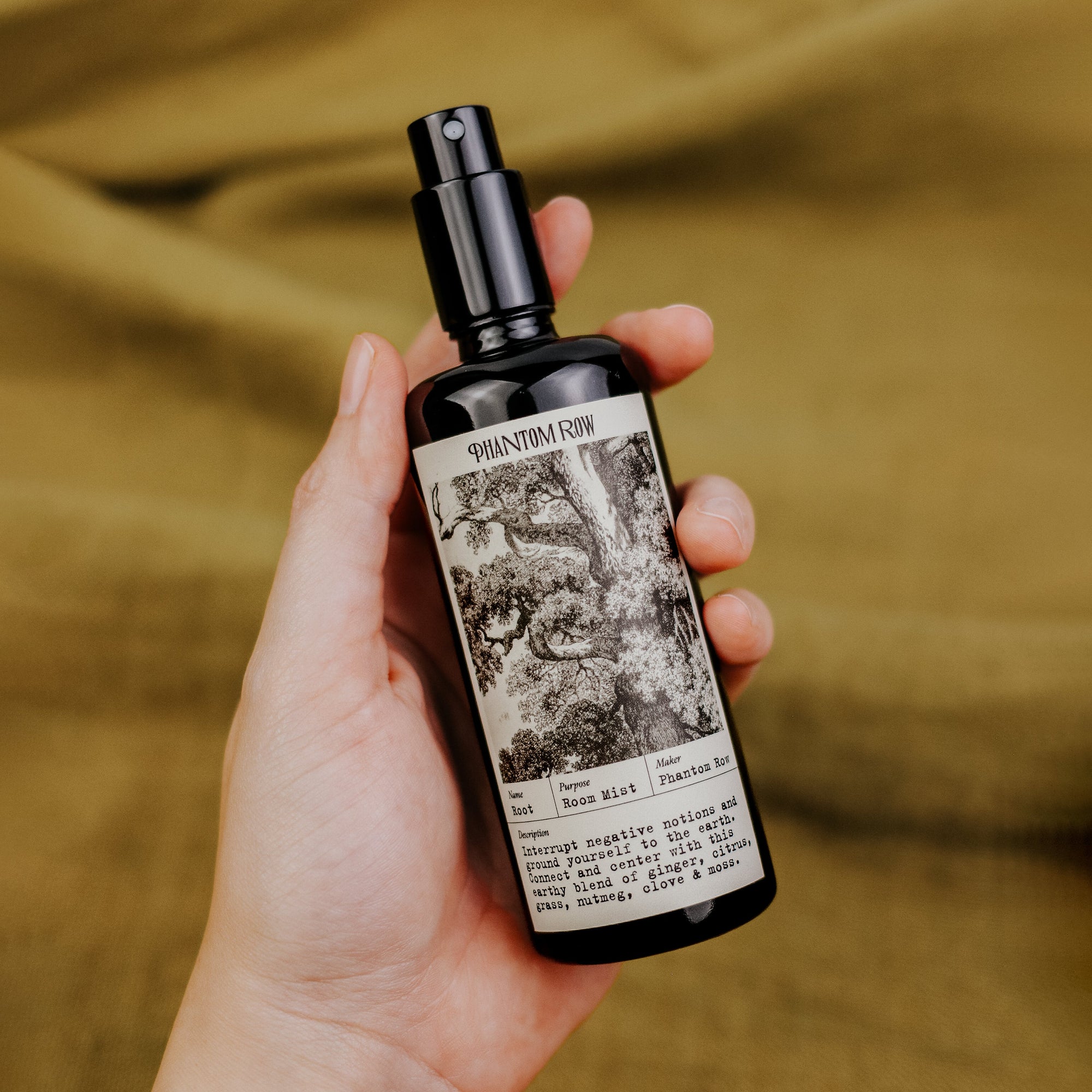 Hand holding a bottle of 'Phantom Row' with a label featuring black and white imagery on a blurred background.