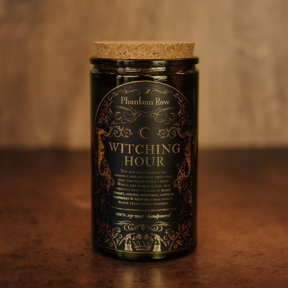 Candle jar labeled 'Witching Hour' by Phantom Row on a wooden surface with a blurred background.