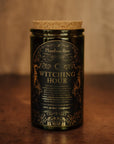 Candle jar labeled 'Witching Hour' by Phantom Row on a wooden surface with a blurred background.